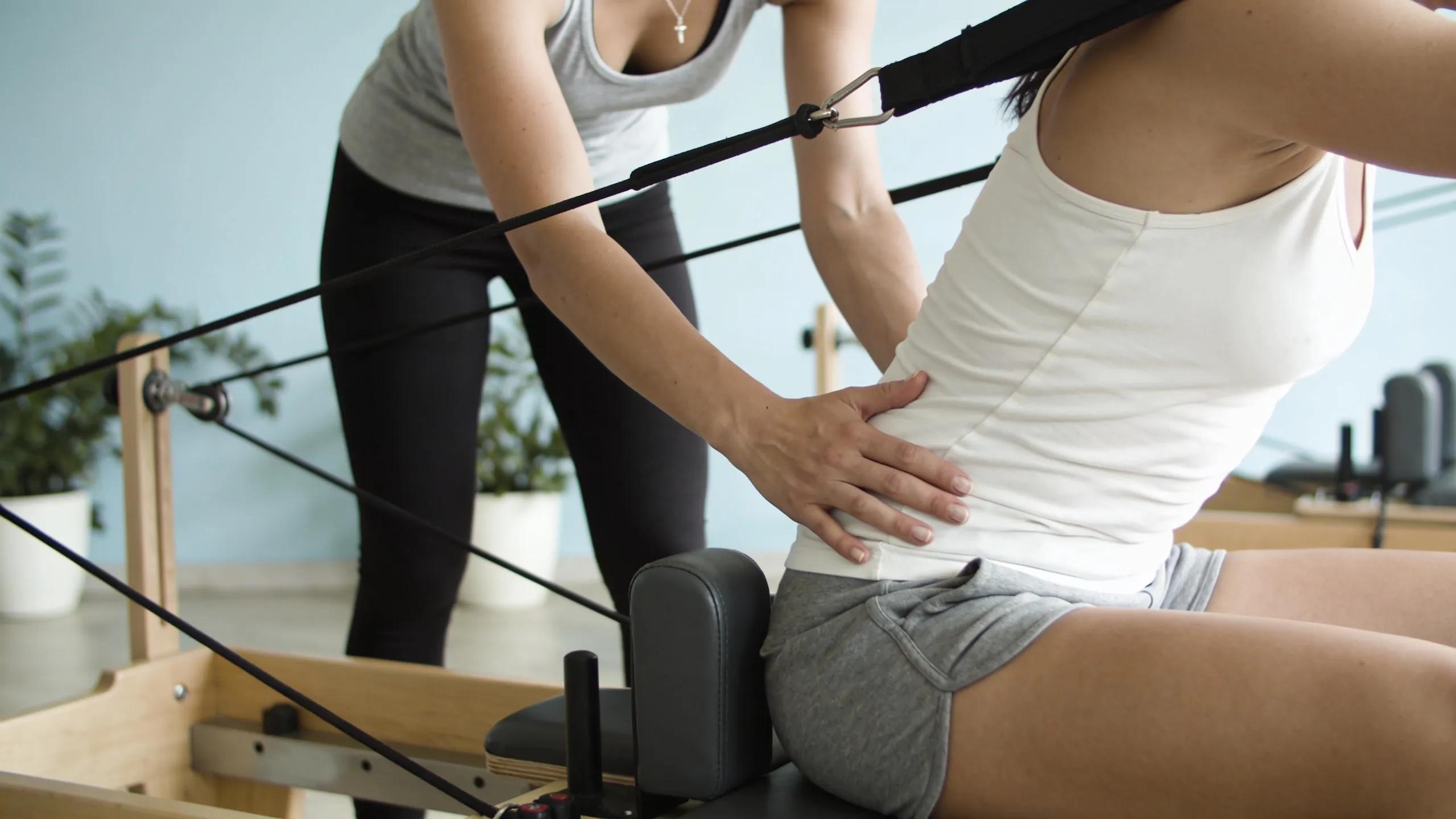 Pilates instructor assisting a client with neuromuscular re-education on a Reformer for pain reduction